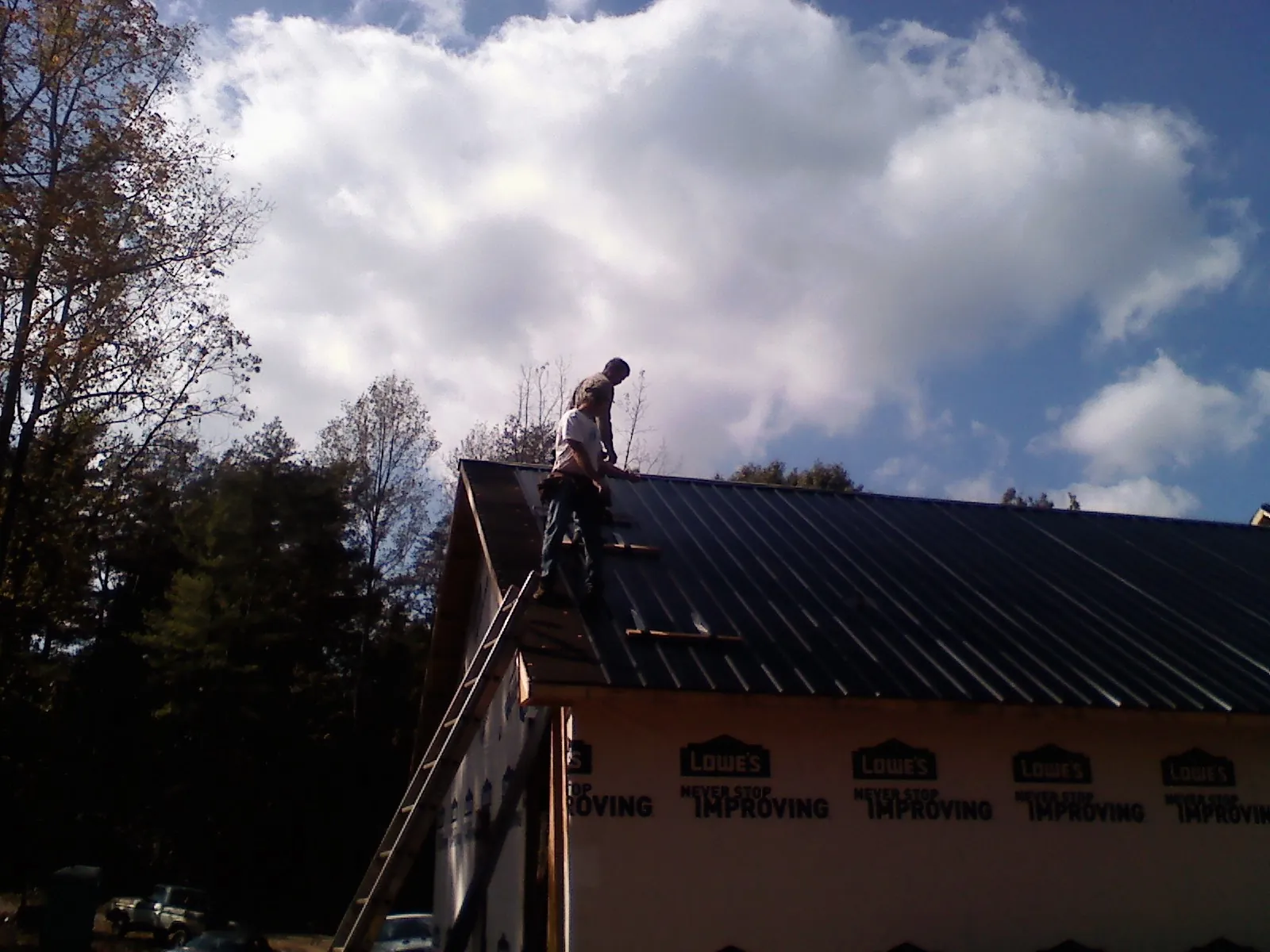 Roofer fastening dark metal panels high against a cloudy sky, from a Roof Inspection job in Stevensville
