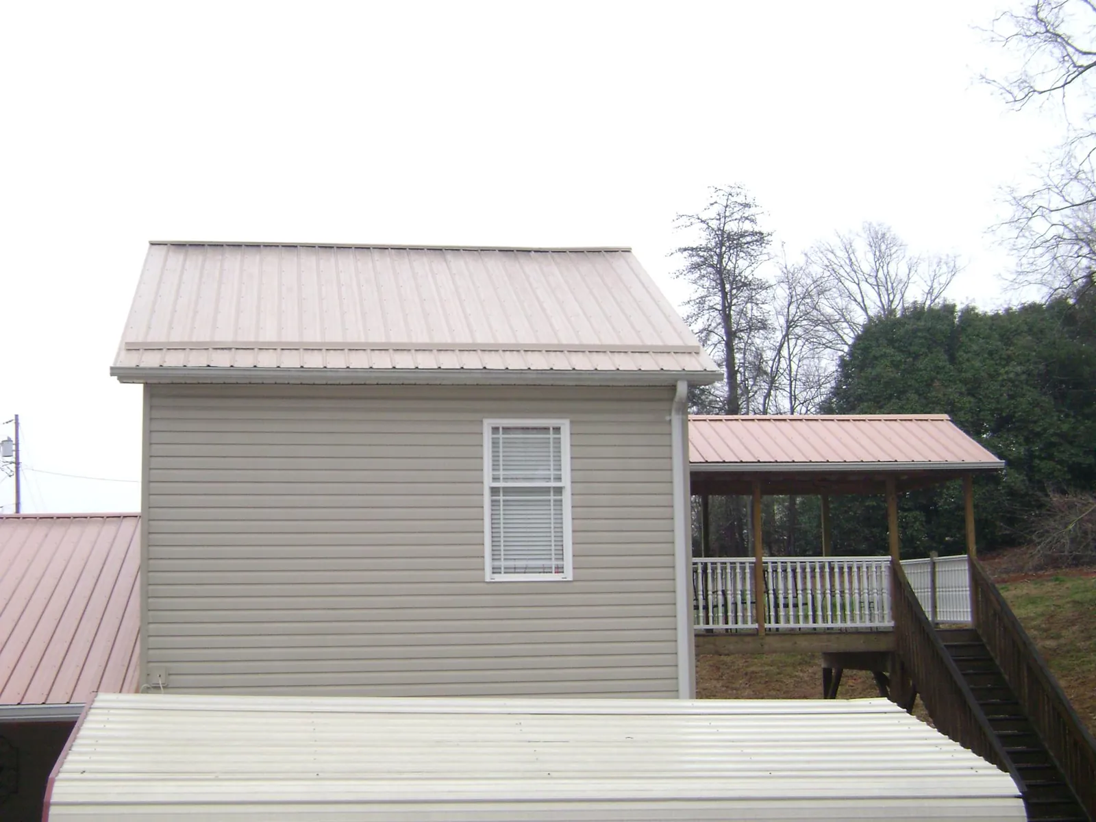 Tan metal roofs on a two story addition and attached porch, from a Roof Replacement job in Stevensville